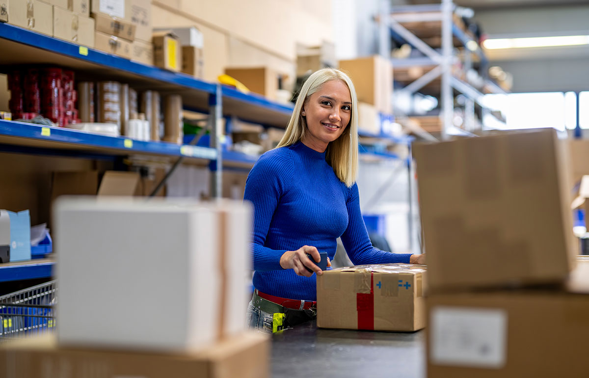 Eine Mitarbeiterin arbeitet an einem Förderband in der Versandstation. Sie überprüft, scannt und sortiert die Pakete.